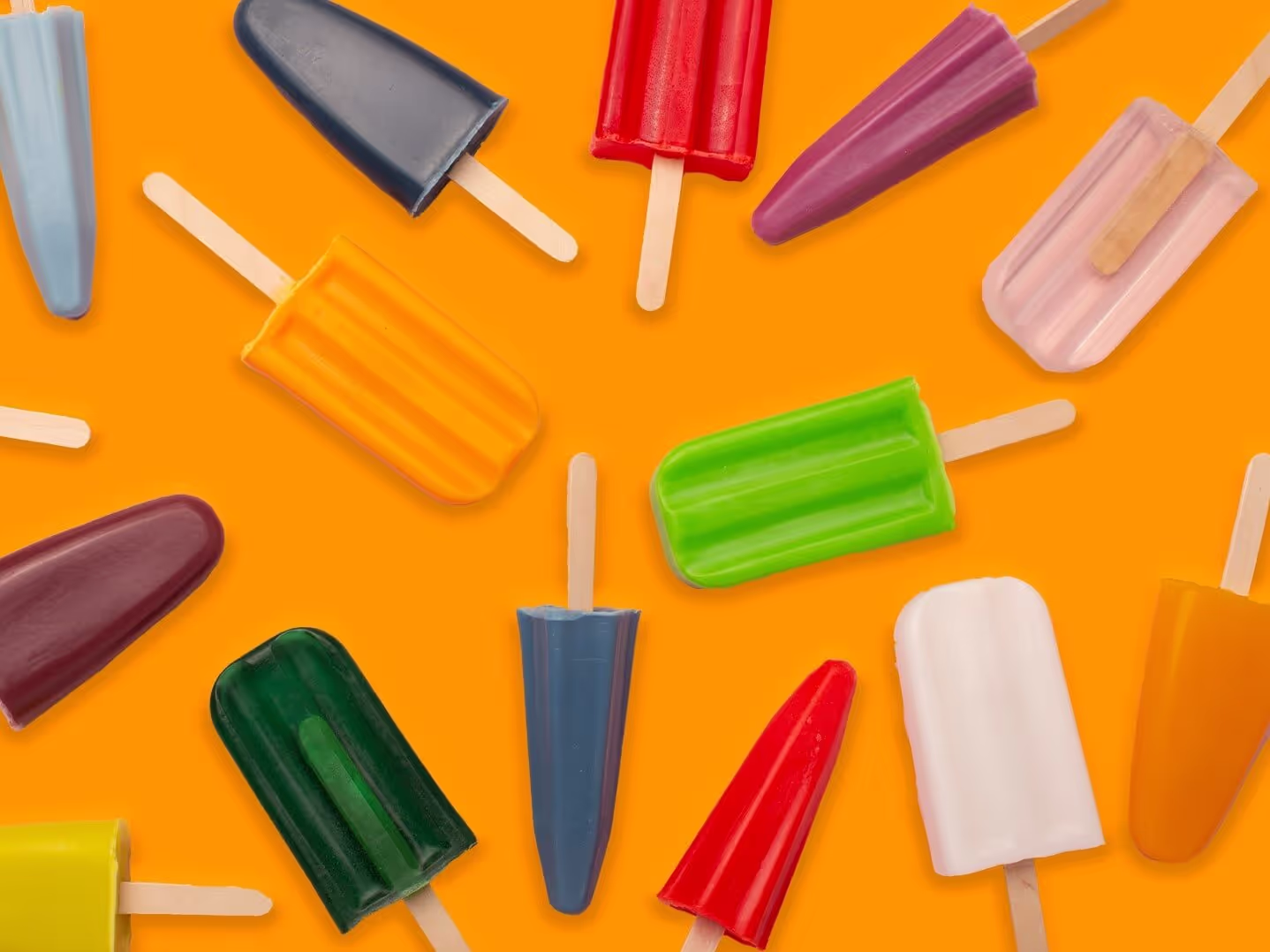 Bunte Eis am Stiel in verschiedenen Geschmacksrichtungen und Schattierungen sind auf einem leuchtend orangefarbenen Hintergrund verstreut, jeder mit einem Holzstab, wodurch ein lustiges und lebhaftes Sommermotiv entsteht.